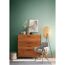 Holzkommode, Stehlampe, Sessel und Deko vor grüner Wand