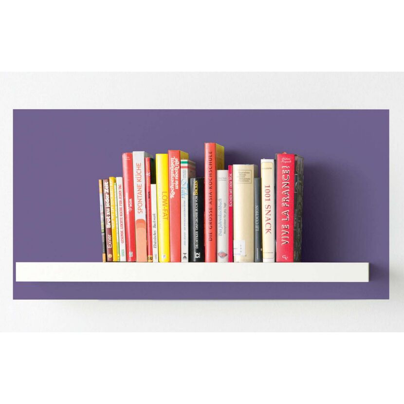 Kochbücher stehen in einem weißen Regal vor lilafarbener Wand.
