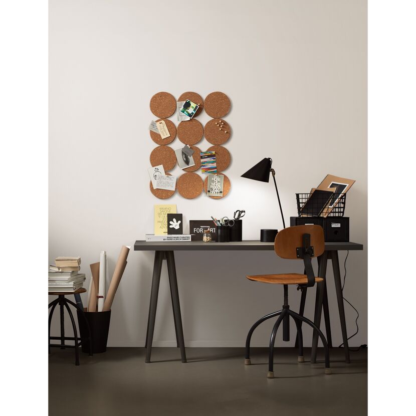 Ein aufgeräumter Schreibtisch mit Pinnwand, Lampe und Notizbüchern.