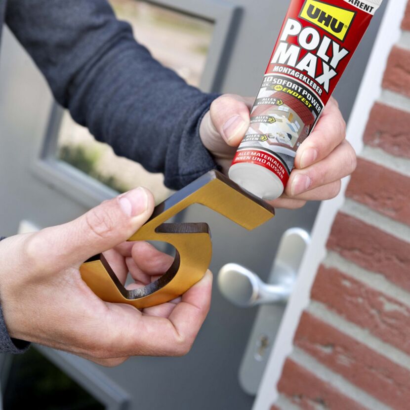 Person trägt UHU Poly Max Montagekleber auf goldene Hausnummer 5 auf