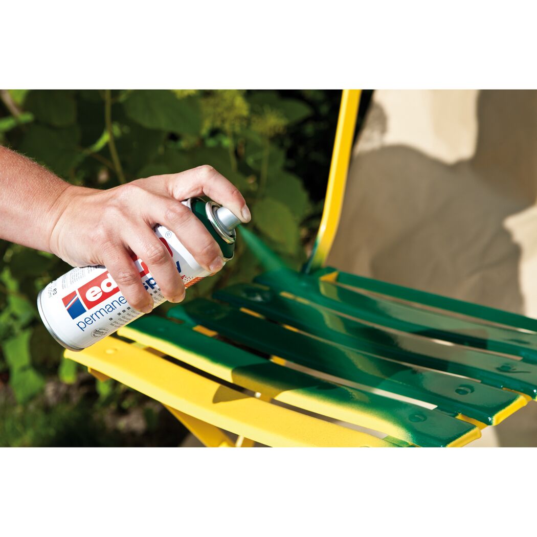 Person sprüht grünen Lack auf Gartenstuhl