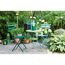 Zwei grüne und ein blauer Klappstuhl, ein Tisch und Deko im Garten.