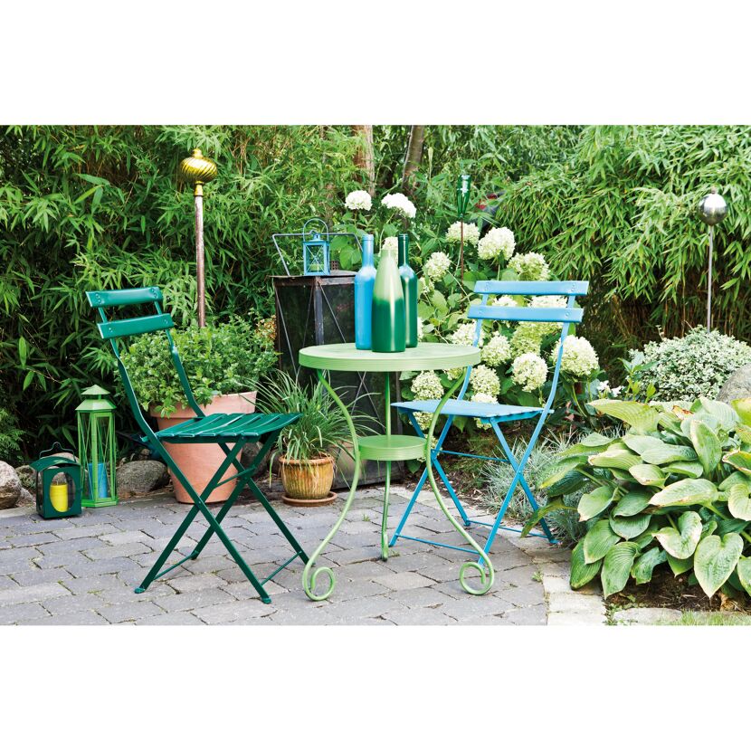 Zwei grüne und ein blauer Klappstuhl, ein Tisch und Deko im Garten.