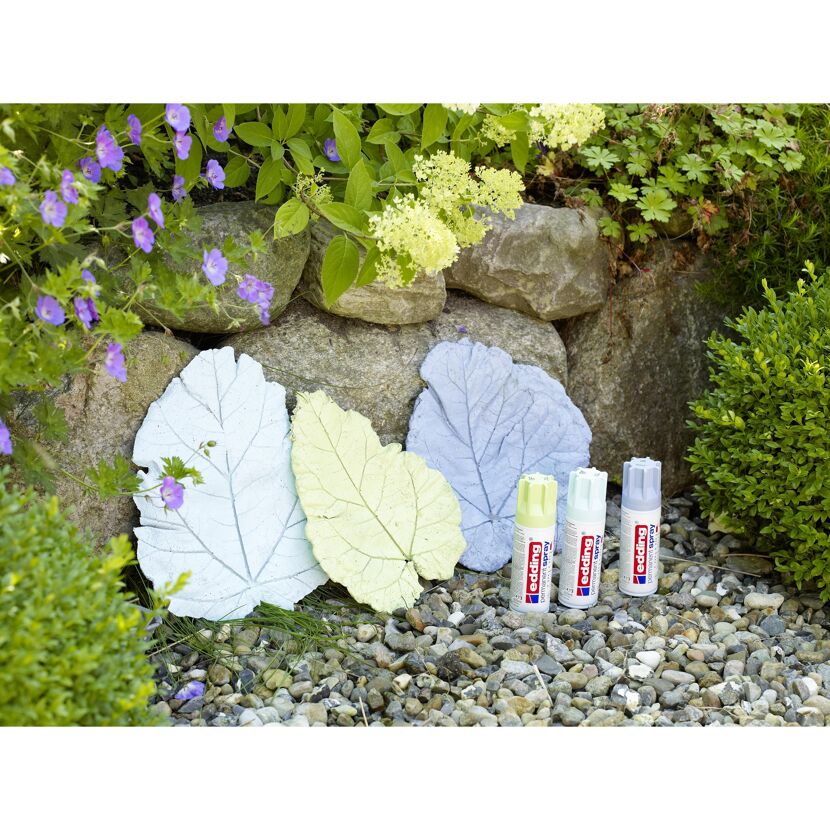 Drei Sprühdosen edding Permanentspray neben drei besprühten Blättern