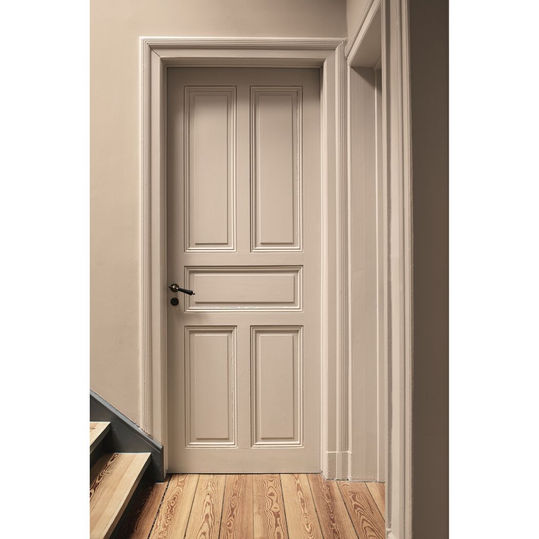 Geschlossene beige Tür in einem Flur mit Holzboden und Treppe.