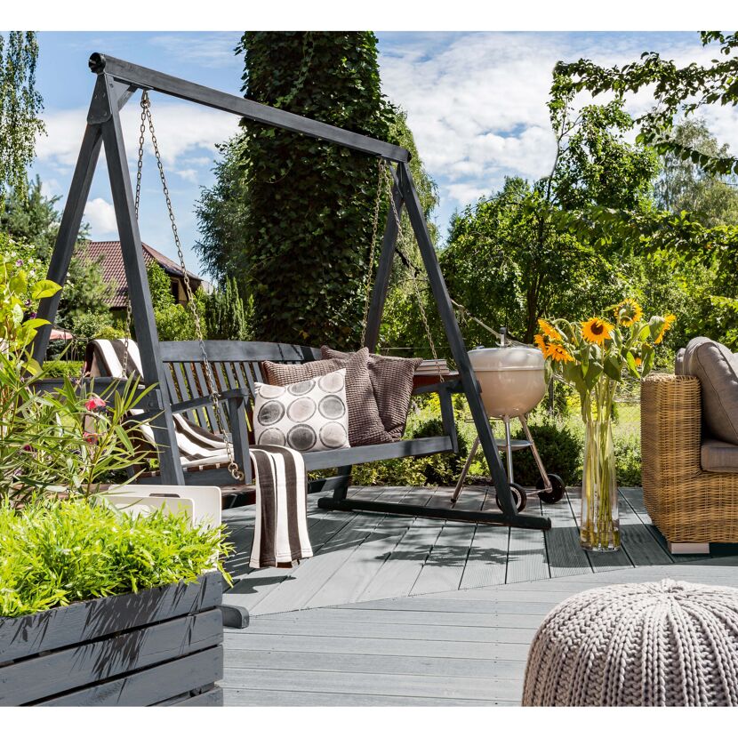 Graue Gartenschaukel auf Terrasse mit Grill und Sonnenblumen