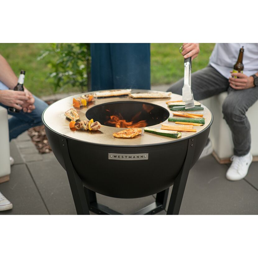 Personen grillen Gemüse und Fleisch auf einer Feuerstelle.