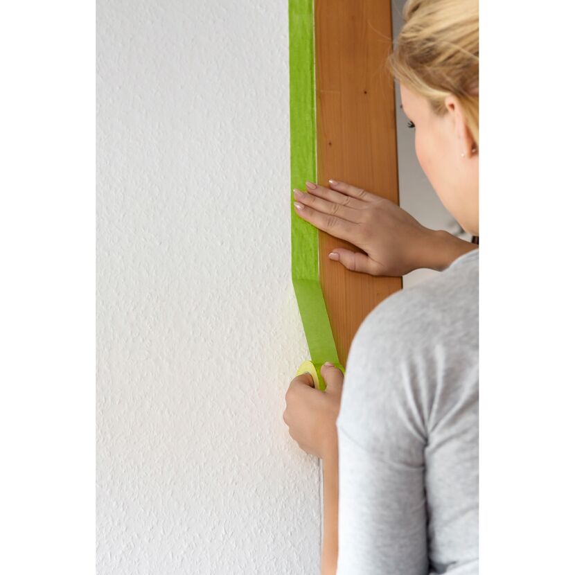Person klebt Frogtape auf eine weiße Wand.