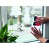 Person bringt Weihnachtsdeko mit Rakel an Fenster an