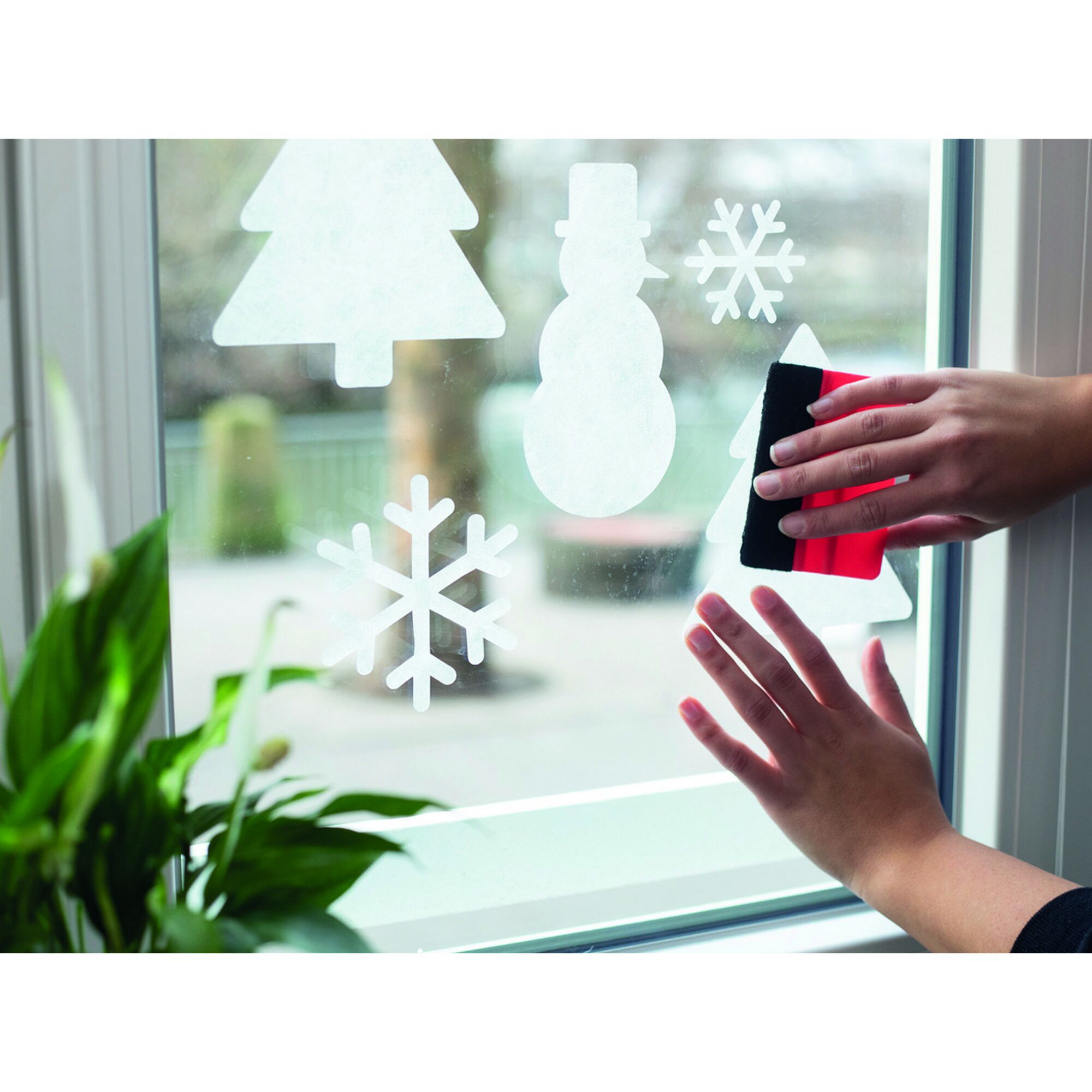 Person bringt Weihnachtsdeko mit Rakel an Fenster an