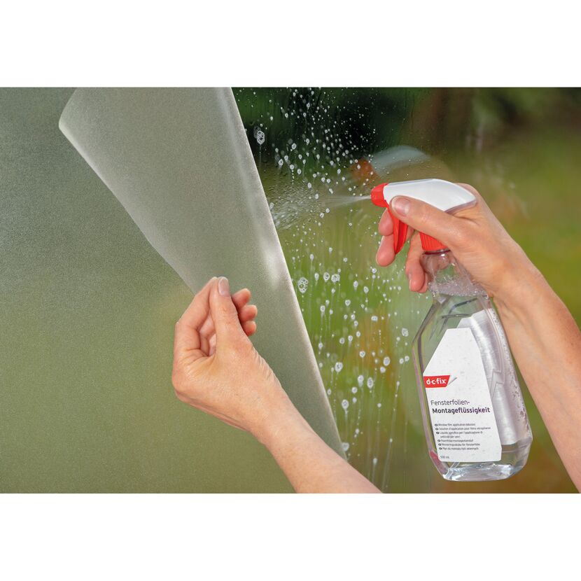 Person bringt Fensterfolie mit Sprühflasche an