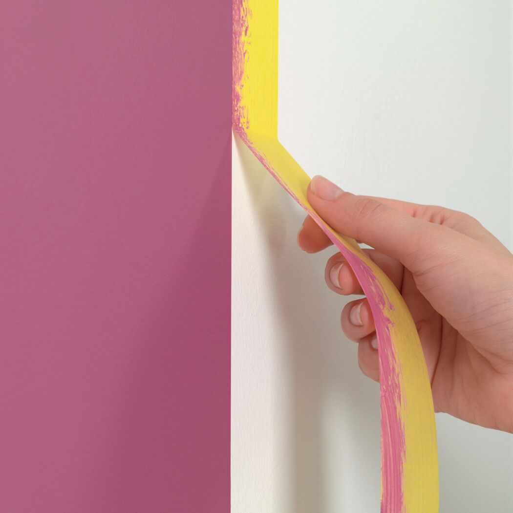 Person entfernt Malerband von einer Wand
