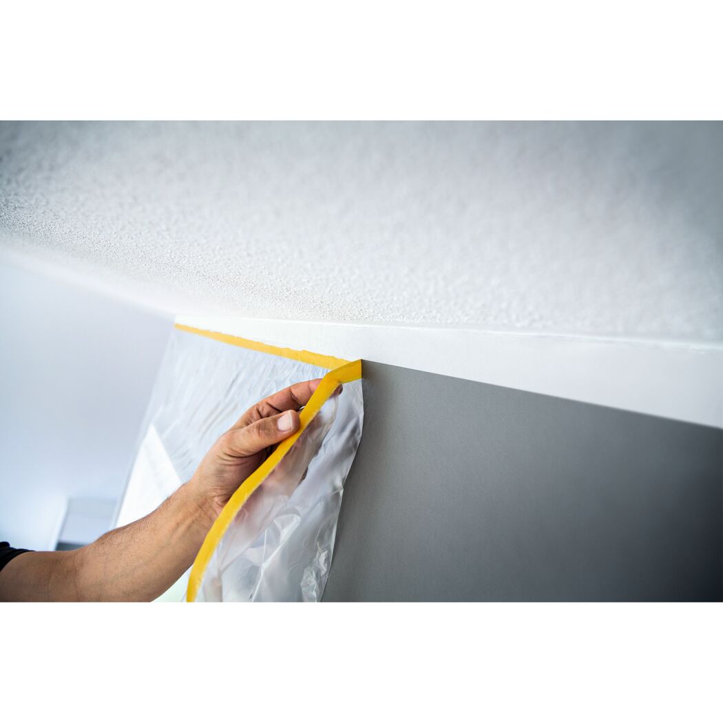 Person klebt gelbes Kreppband an eine Wand.
