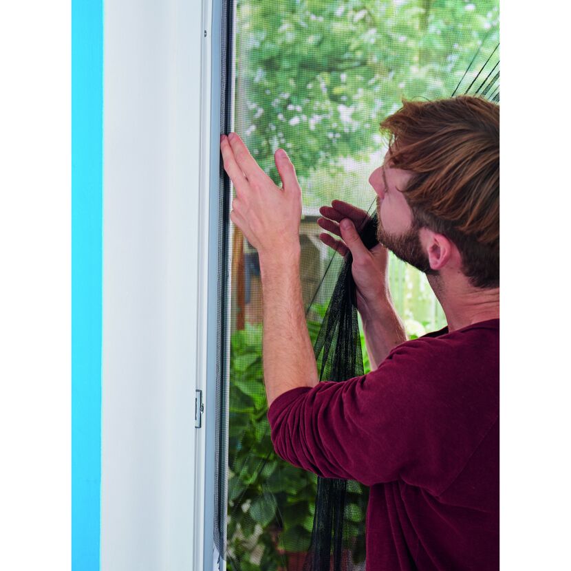 Person bringt Klettband für Fliegengitter am Fenster an.