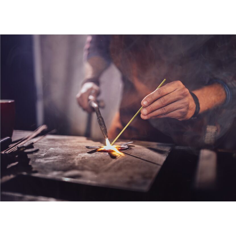 Person lötet mit einem Gasbrenner ein Metallstück.