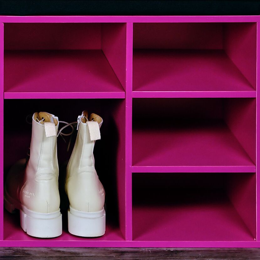 Leere pinke Schuhregal mit einem Paar weißen Stiefeletten