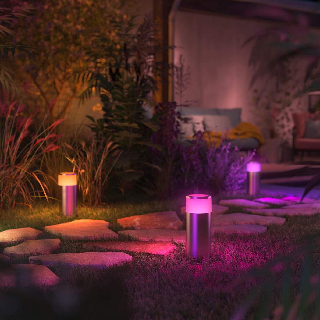 Wegeleuchten 'Hue Calla' beleuchten farbigen Gartenweg bei Nacht.
