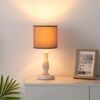 Eine kleine Tischlampe mit beigem Lampenschirm leuchtet.