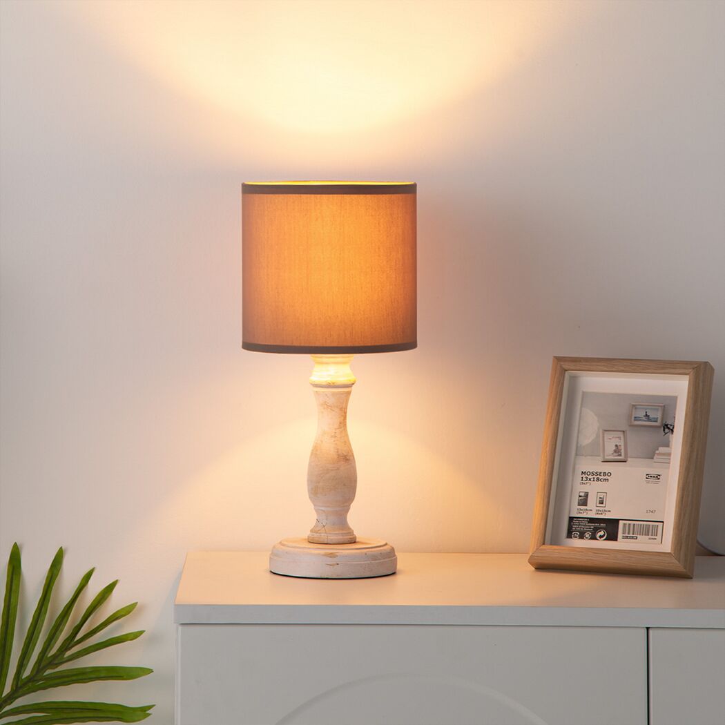 Eine kleine Tischlampe mit beigem Lampenschirm leuchtet.