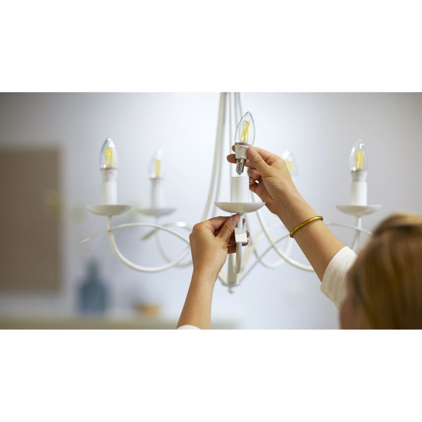 Person schraubt eine Philips Smart LED E14, C35, 40W, CL in einen Kronleuchter.