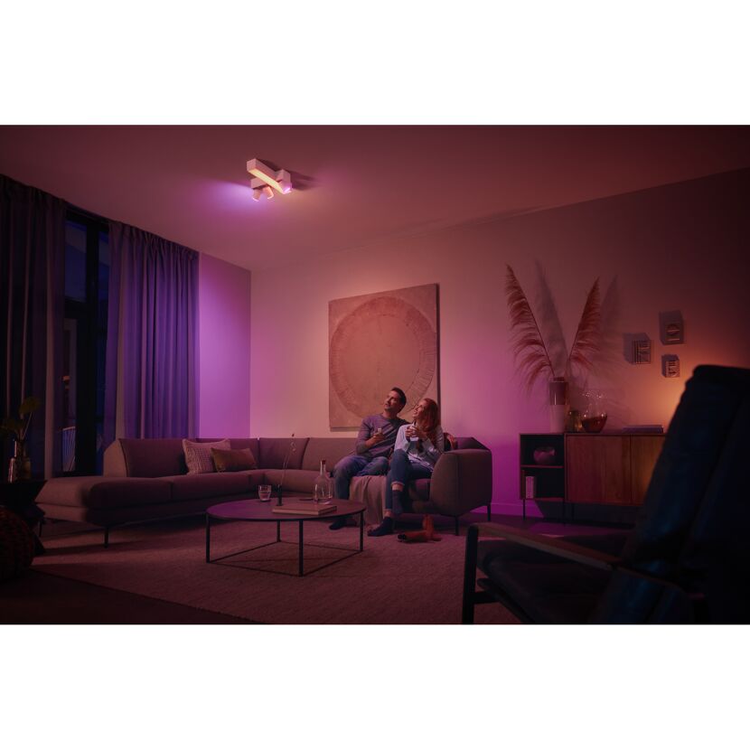 Paar bedient 'Hue' Dimmschalter in stimmungsvollem Wohnzimmer.