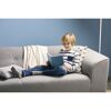 Kind liest Buch auf grauem Sofa.