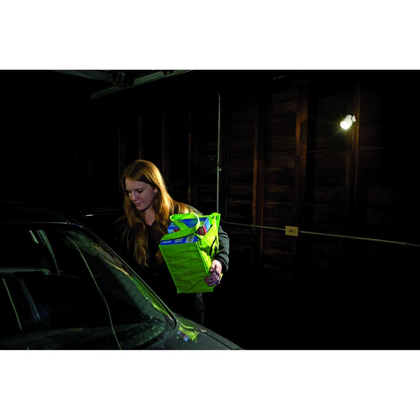 Person trägt grüne Einkaufstasche zum Auto
