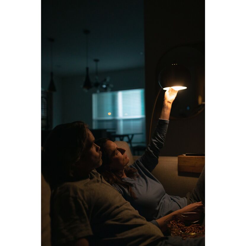 Zwei Personen sitzen auf einem Sofa und eine Person schaltet eine Lampe ein.