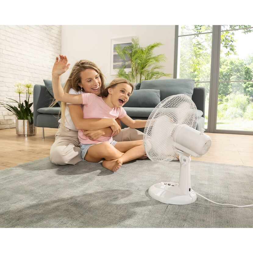 Person und Kind sitzen vor einem Ventilator.