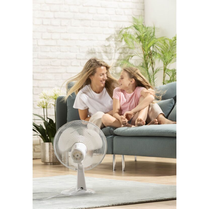 Person und Kind sitzen auf Sofa, Ventilator im Vordergrund