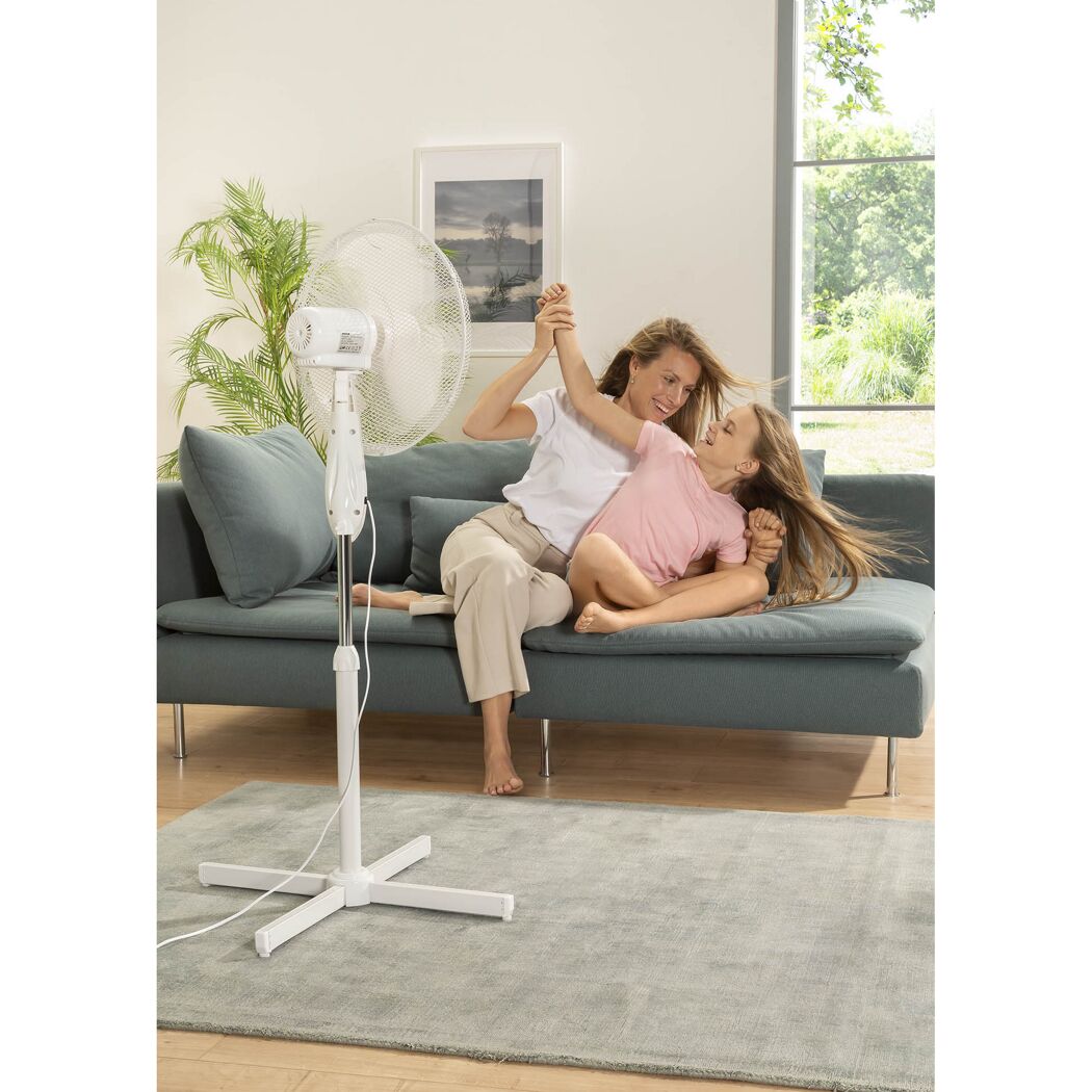 Person und Kind sitzen auf Sofa vor Standventilator