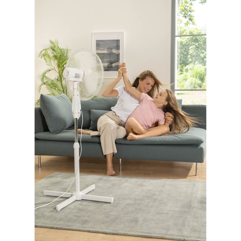 Person und Kind sitzen auf Sofa vor Standventilator