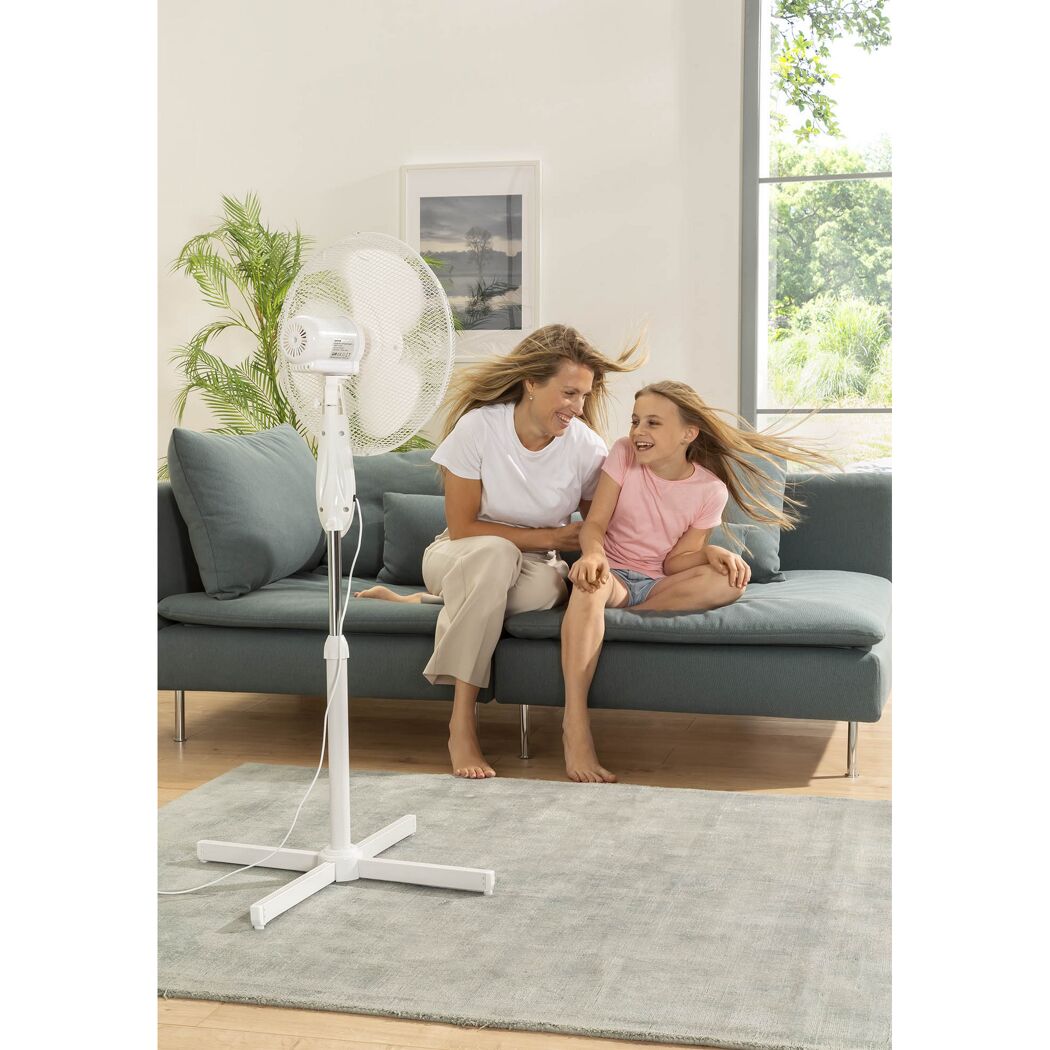 Zwei Personen sitzen auf einem Sofa vor einem Standventilator.