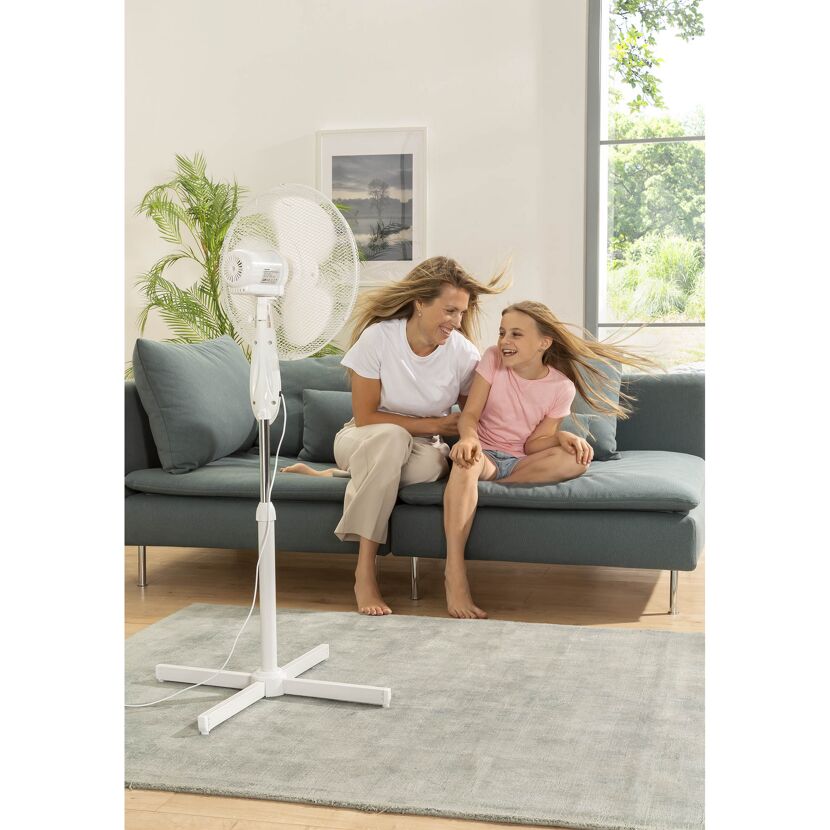 Zwei Personen sitzen auf einem Sofa vor einem Standventilator.