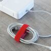 Weißes Netzteil und aufgerolltes Kabel mit rotem Klettverschluss.