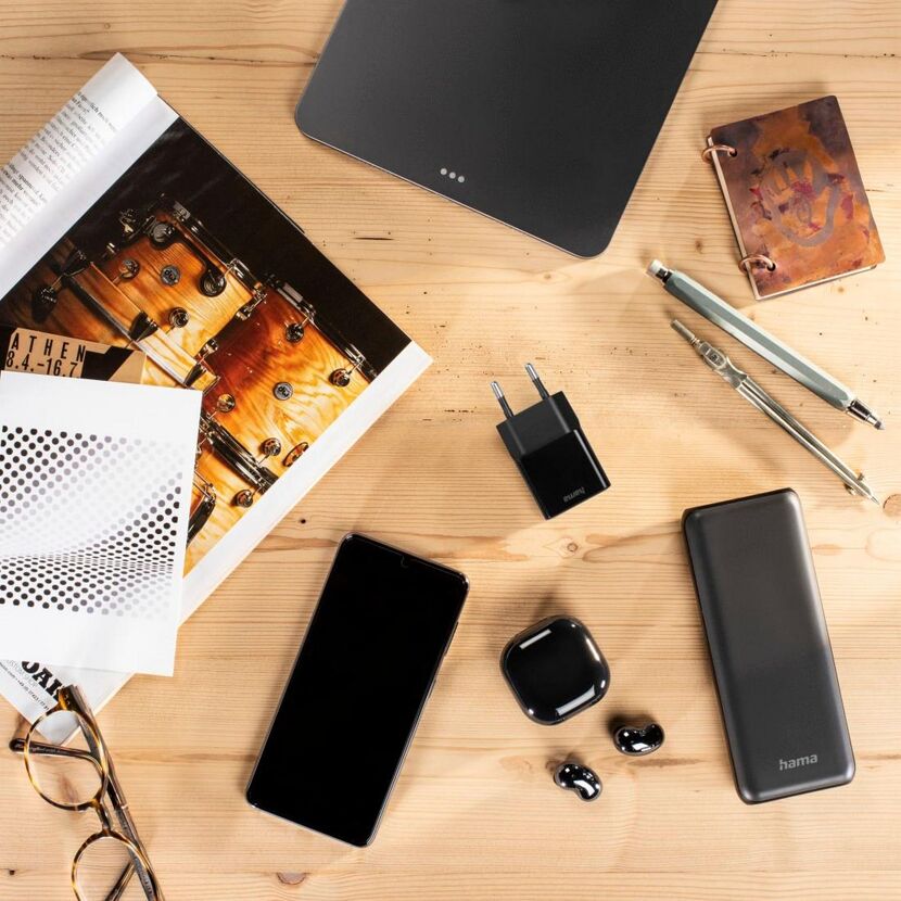 Smartphone, Kopfhörer, Ladegerät und Powerbank auf Tisch.