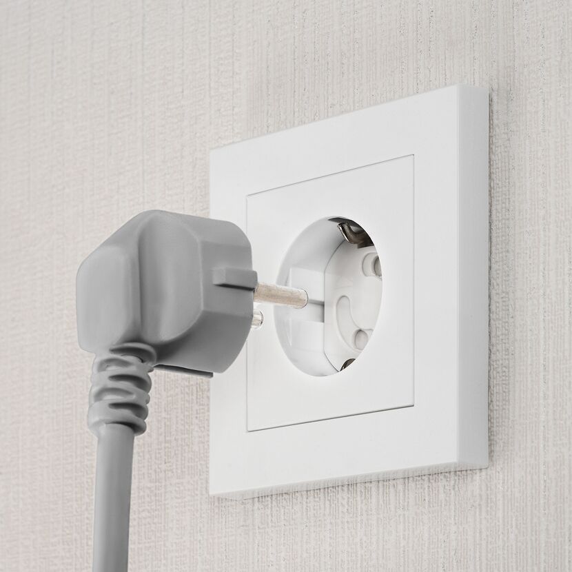 Grauer Stecker wird in eine weiße Steckdose gesteckt.