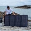 Person baut Solarpanel am Meer auf.