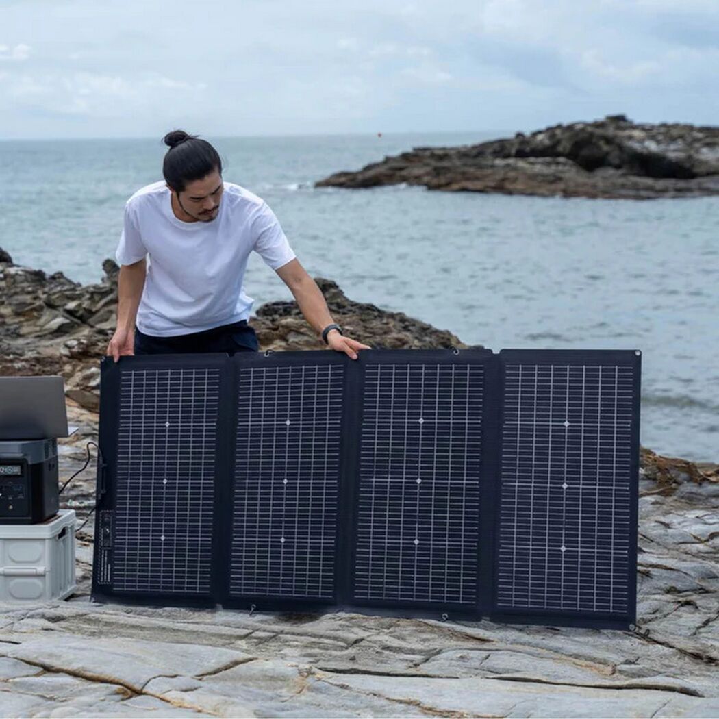 Person baut Solarpanel am Meer auf.