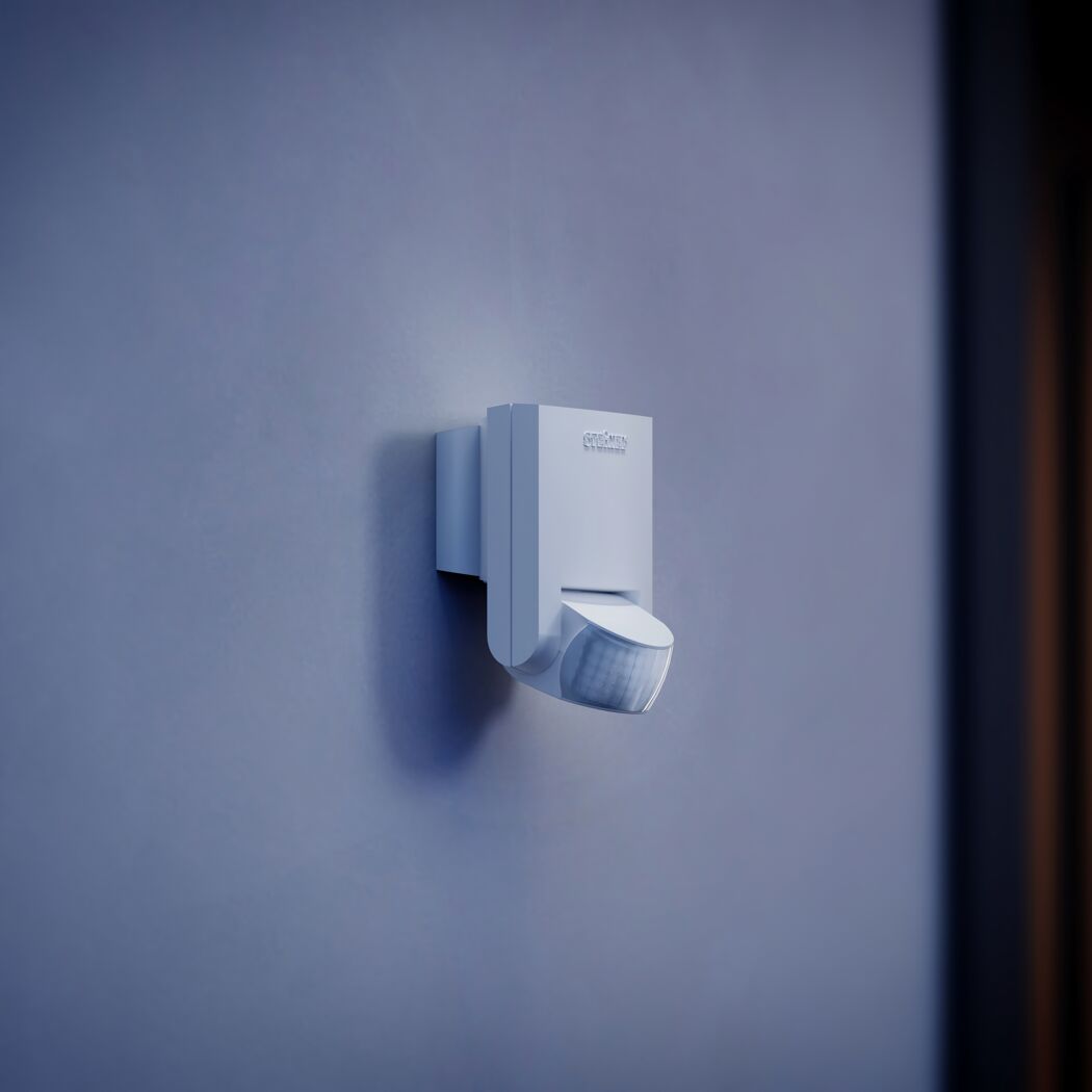 Weißer STEINEL Bewegungsmelder an blauer Wand.