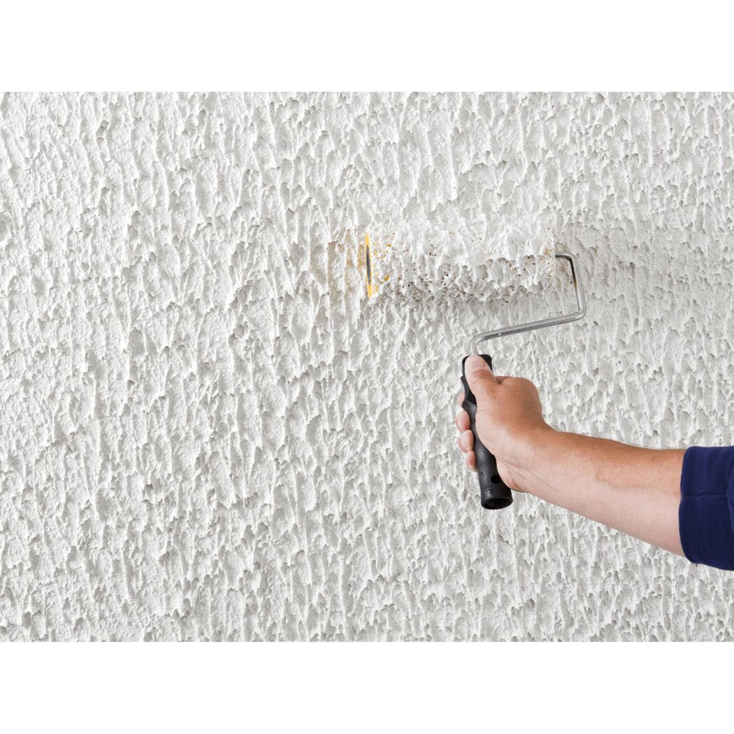 Person streicht eine Wand mit Reibeputz mit einer Farbrolle.