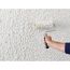 Person streicht eine Wand mit Reibeputz mit einer Farbrolle.