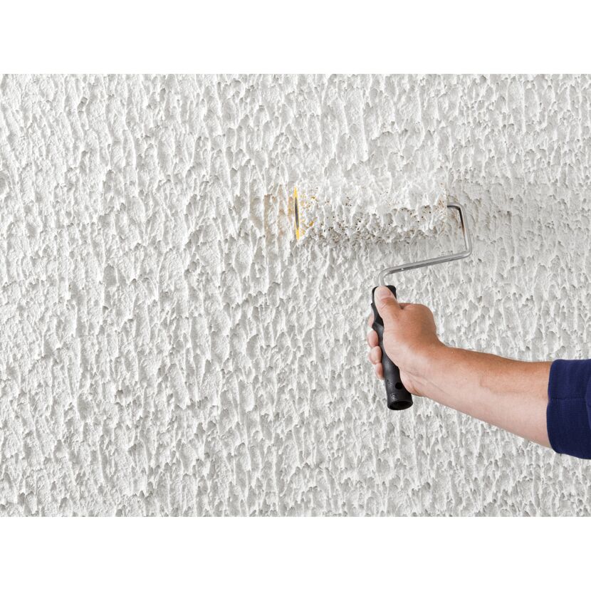 Person streicht eine Wand mit Reibeputz mit einer Farbrolle.