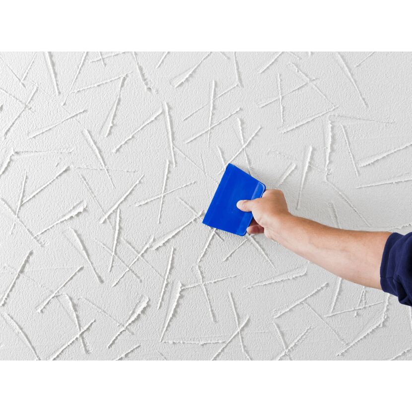 Person verputzt eine Wand mit einem blauen Spachtel.