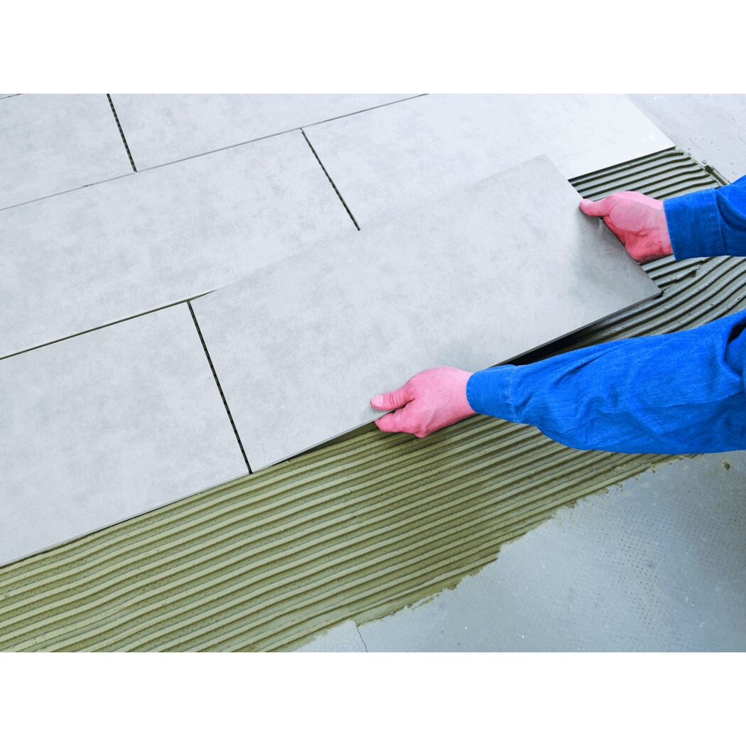 Person verlegt graue Fliesen mit Fliesenkleber.